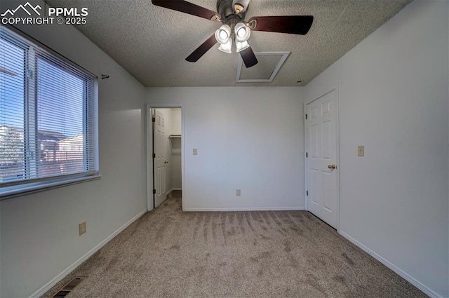 unfurnished bedroom with ceiling fan, a closet, light colored carpet, a textured ceiling, and a walk in closet