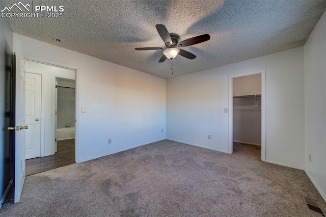 unfurnished bedroom featuring a spacious closet, carpet, a textured ceiling, a closet, and ceiling fan