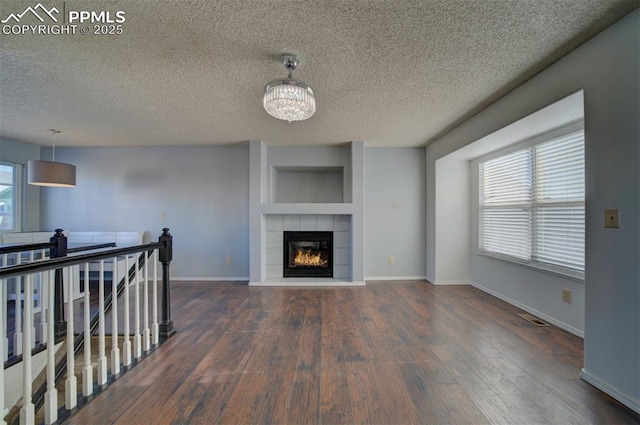 unfurnished living room with a tiled fireplace, dark wood-type flooring, a chandelier, and a textured ceiling