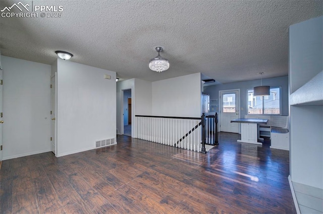 spare room with a textured ceiling, dark wood-type flooring, and an inviting chandelier