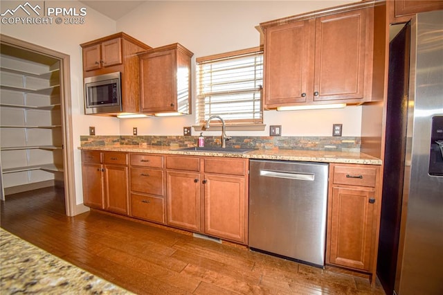 kitchen with sink, stainless steel appliances, light stone counters, and wood-type flooring