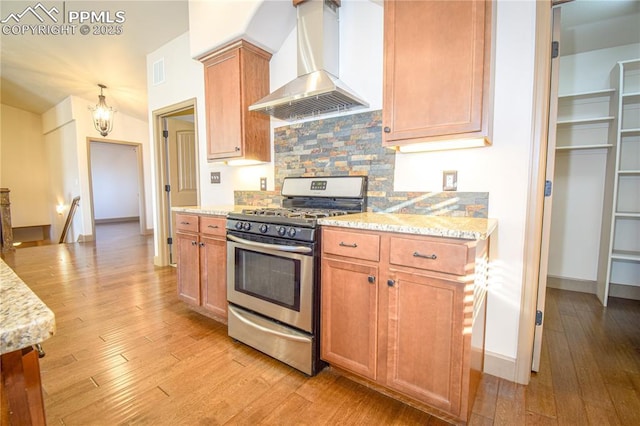 kitchen with exhaust hood, light stone countertops, decorative backsplash, light hardwood / wood-style flooring, and stainless steel range with gas stovetop