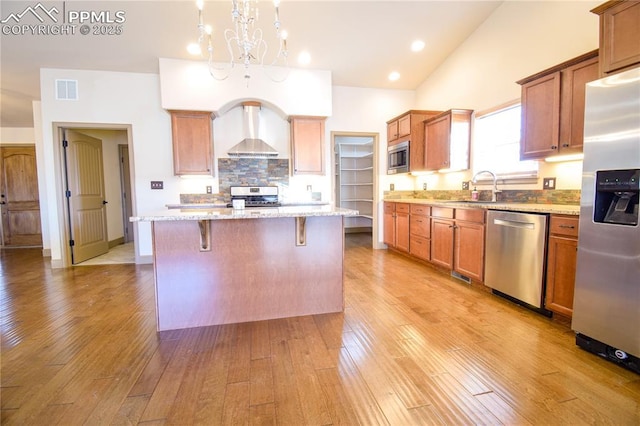 kitchen featuring appliances with stainless steel finishes, sink, a kitchen island, pendant lighting, and wall chimney exhaust hood