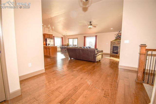 living room featuring light hardwood / wood-style floors, ceiling fan with notable chandelier, lofted ceiling, and a fireplace