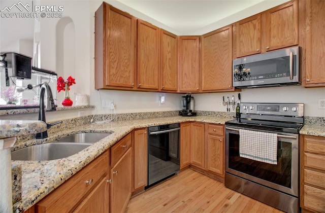 kitchen with sink, light hardwood / wood-style floors, light stone counters, and appliances with stainless steel finishes