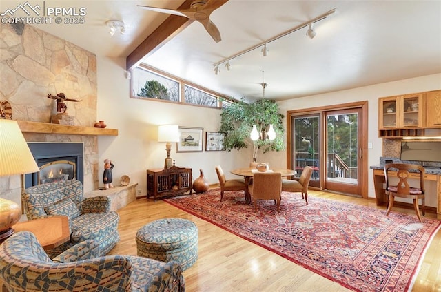 living room with ceiling fan with notable chandelier, a fireplace, lofted ceiling with beams, and light hardwood / wood-style flooring