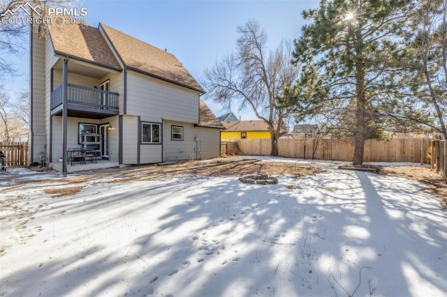 snow covered rear of property with a balcony and a fire pit