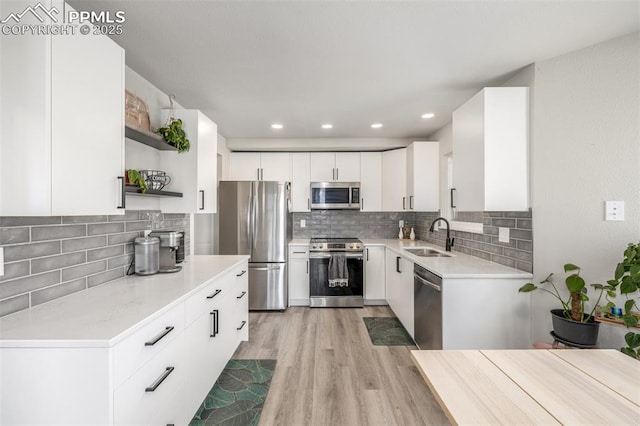 kitchen with appliances with stainless steel finishes, sink, light wood-type flooring, white cabinetry, and decorative backsplash