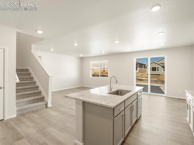 kitchen with light hardwood / wood-style floors, gray cabinetry, a kitchen island with sink, light stone counters, and sink