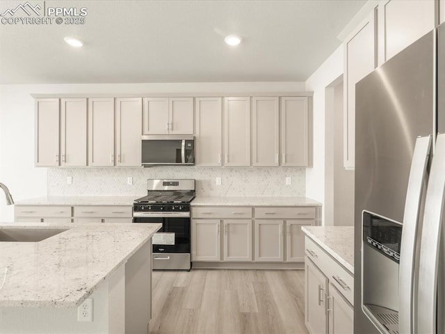 kitchen featuring light hardwood / wood-style floors, appliances with stainless steel finishes, light stone countertops, white cabinets, and sink