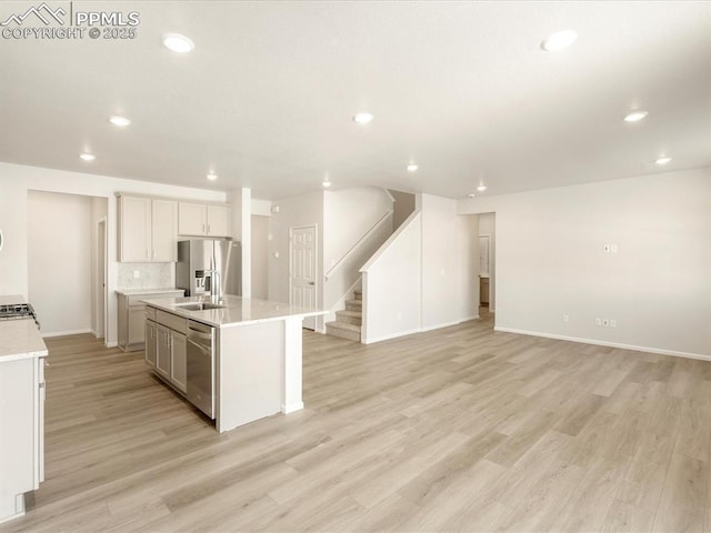 kitchen with white cabinets, stainless steel appliances, light hardwood / wood-style floors, sink, and a kitchen island with sink