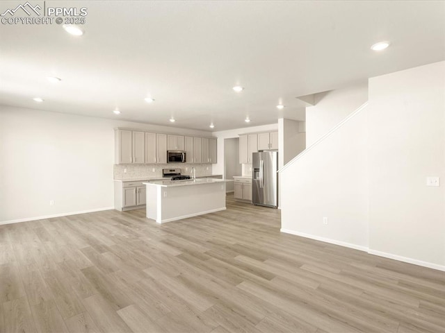 kitchen with a kitchen bar, a center island with sink, appliances with stainless steel finishes, tasteful backsplash, and light wood-type flooring