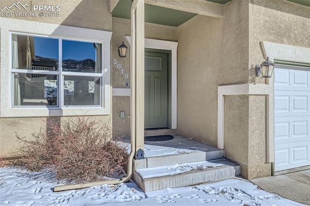 snow covered property entrance featuring a garage