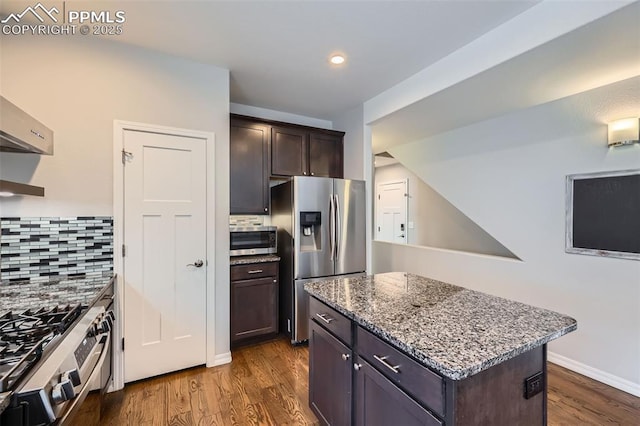 kitchen with stainless steel appliances, light stone countertops, a center island, decorative backsplash, and dark brown cabinetry