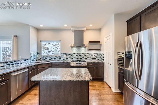 kitchen featuring wall chimney exhaust hood, sink, light stone countertops, a center island, and stainless steel appliances