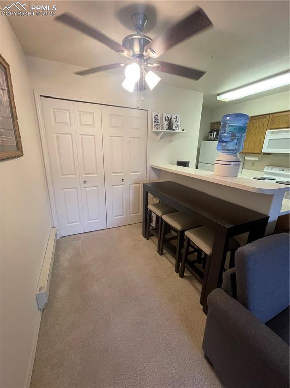 interior space featuring light colored carpet, a breakfast bar, kitchen peninsula, white appliances, and a baseboard radiator