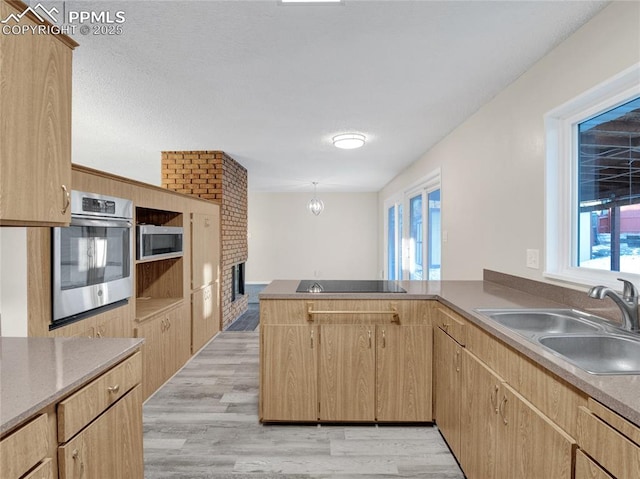 kitchen featuring light hardwood / wood-style floors, kitchen peninsula, appliances with stainless steel finishes, light brown cabinetry, and sink