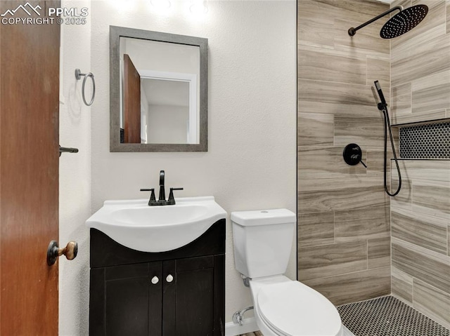 bathroom featuring toilet, tiled shower, and vanity