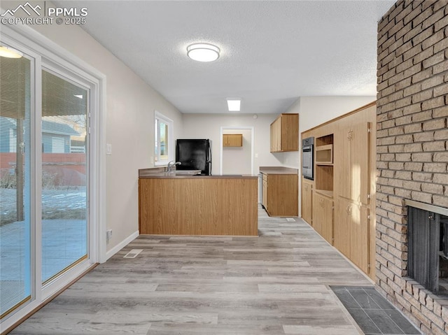 kitchen featuring light hardwood / wood-style floors, kitchen peninsula, black refrigerator, a brick fireplace, and a textured ceiling