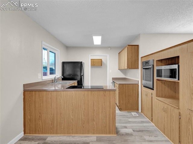 kitchen with black appliances, kitchen peninsula, sink, light wood-type flooring, and a textured ceiling