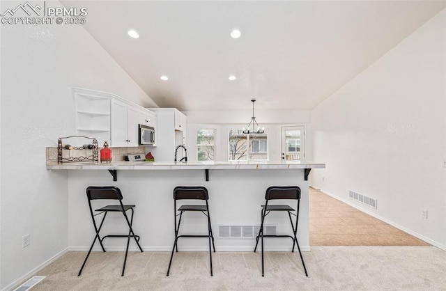 kitchen featuring white cabinetry, kitchen peninsula, backsplash, vaulted ceiling, and a breakfast bar