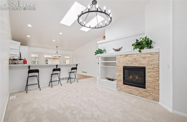 carpeted living room with vaulted ceiling with skylight and a stone fireplace