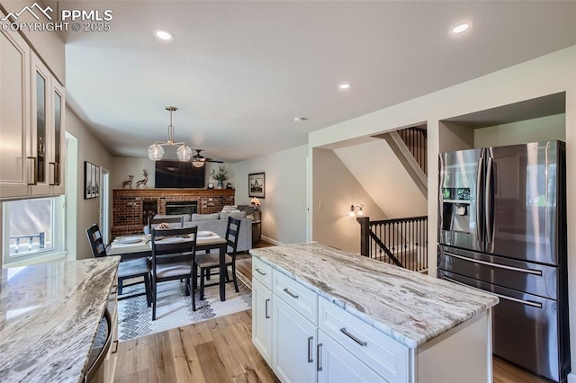 kitchen with white cabinetry, stainless steel fridge, light hardwood / wood-style flooring, light stone counters, and a center island