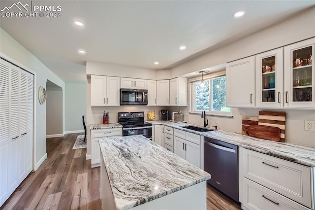 kitchen with a kitchen island, white cabinetry, stainless steel appliances, sink, and light stone counters