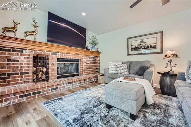 living room featuring a brick fireplace, hardwood / wood-style floors, and ceiling fan