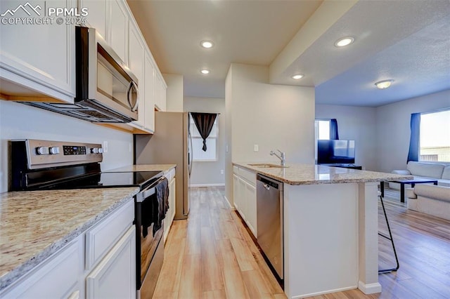 kitchen featuring sink, a breakfast bar, appliances with stainless steel finishes, white cabinetry, and light stone countertops