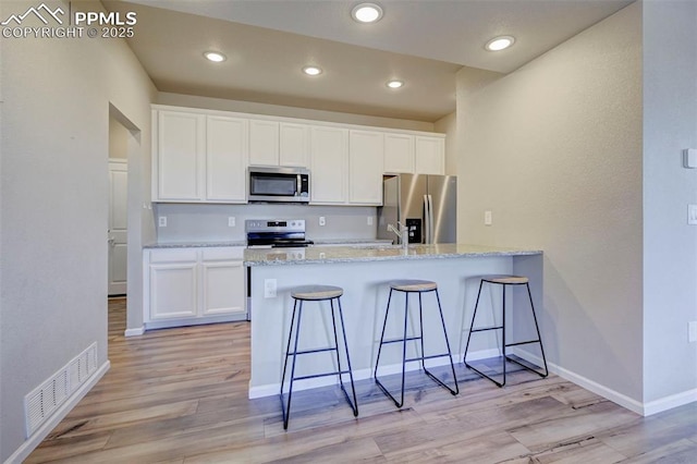 kitchen featuring white cabinetry, stainless steel appliances, light stone countertops, and light wood-type flooring