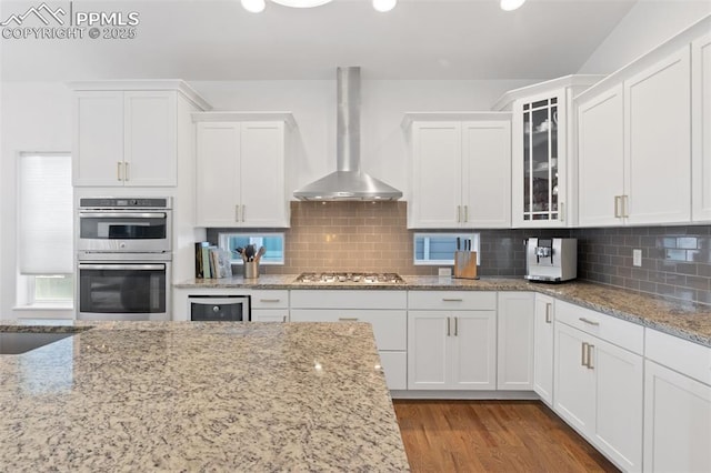 kitchen with tasteful backsplash, wall chimney exhaust hood, stainless steel appliances, and white cabinetry