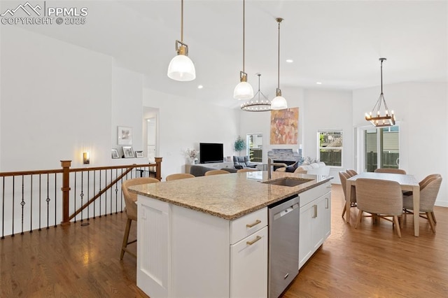 kitchen featuring white cabinetry, stainless steel dishwasher, decorative light fixtures, and a kitchen island with sink