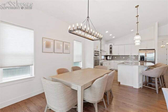 dining room with a chandelier, lofted ceiling, wood-type flooring, and sink