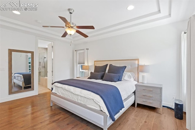 bedroom featuring ceiling fan, connected bathroom, light hardwood / wood-style flooring, and a tray ceiling