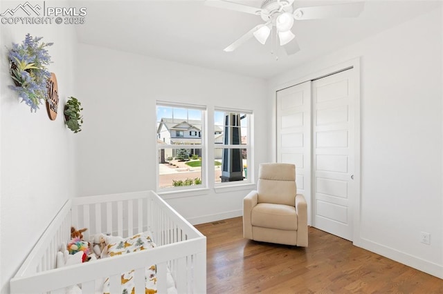 bedroom with ceiling fan, a nursery area, a closet, and wood-type flooring