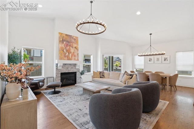 living room with an inviting chandelier, hardwood / wood-style floors, a stone fireplace, and high vaulted ceiling