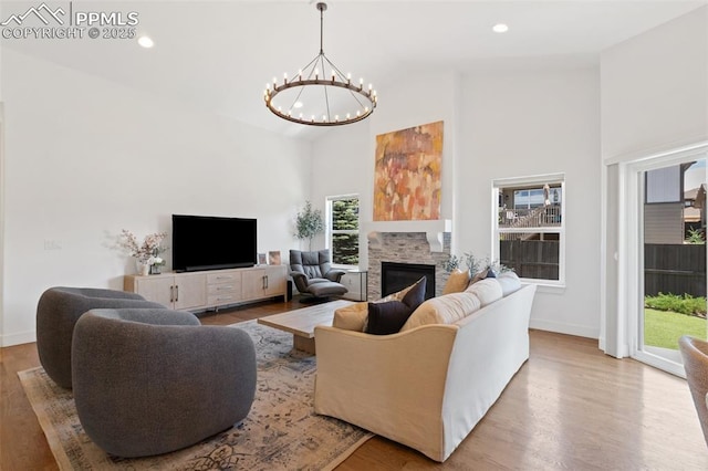 living room with light hardwood / wood-style floors, a towering ceiling, a stone fireplace, and an inviting chandelier