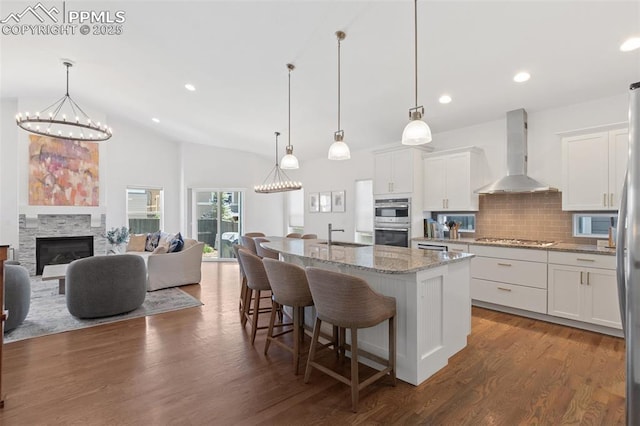 kitchen with decorative backsplash, white cabinets, a center island with sink, and wall chimney exhaust hood