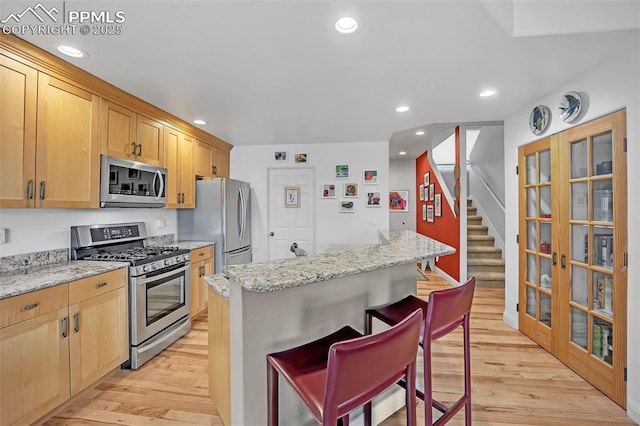 kitchen with a center island, appliances with stainless steel finishes, a kitchen breakfast bar, light hardwood / wood-style flooring, and light stone counters