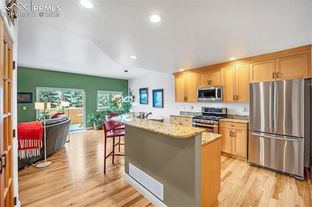 kitchen featuring appliances with stainless steel finishes, a kitchen island with sink, light hardwood / wood-style flooring, light stone counters, and a breakfast bar area