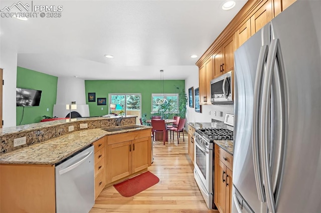 kitchen with light brown cabinets, stainless steel appliances, sink, hanging light fixtures, and light wood-type flooring