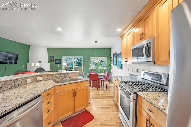 kitchen featuring hanging light fixtures, sink, light wood-type flooring, stainless steel appliances, and light stone counters