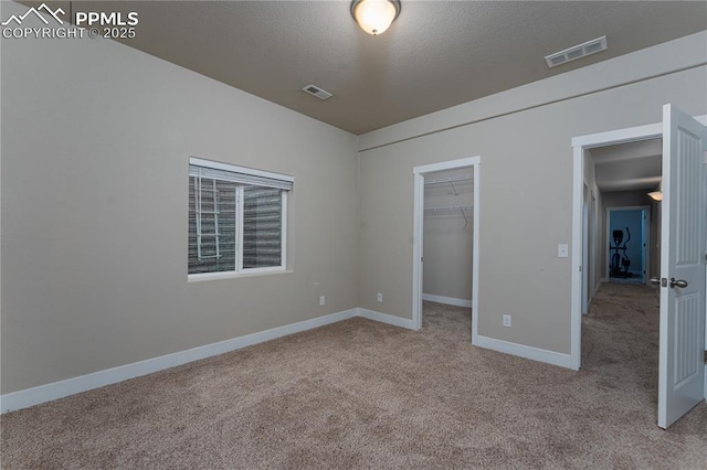 unfurnished bedroom featuring carpet floors, baseboards, a walk in closet, a closet, and a textured ceiling