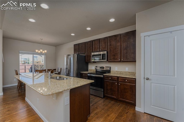 kitchen featuring appliances with stainless steel finishes, a sink, a center island with sink, dark brown cabinetry, and dark wood finished floors