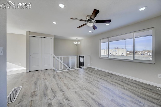 unfurnished room with ceiling fan with notable chandelier and light hardwood / wood-style flooring