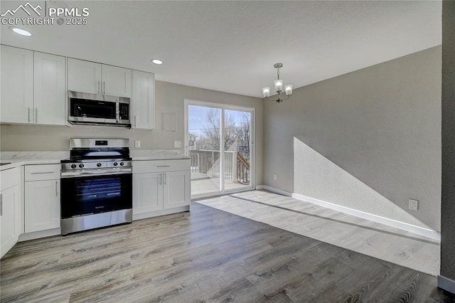 kitchen with an inviting chandelier, white cabinetry, appliances with stainless steel finishes, pendant lighting, and light hardwood / wood-style flooring