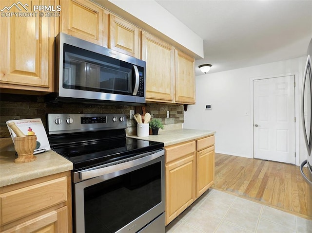 kitchen featuring light brown cabinetry, light tile patterned floors, stainless steel appliances, and tasteful backsplash