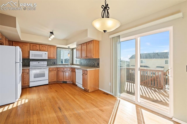 kitchen with decorative backsplash, white appliances, light wood-type flooring, hanging light fixtures, and sink