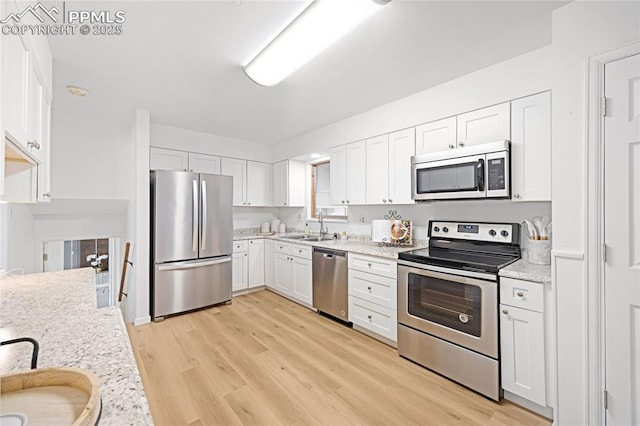 kitchen with stainless steel appliances, white cabinets, light stone countertops, light hardwood / wood-style flooring, and sink